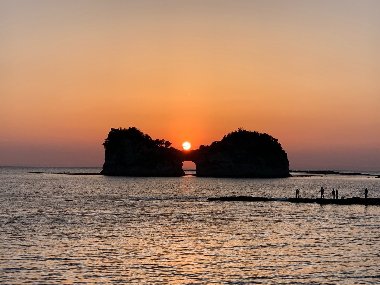中央の穴に夕日が沈む円月島のシルエット