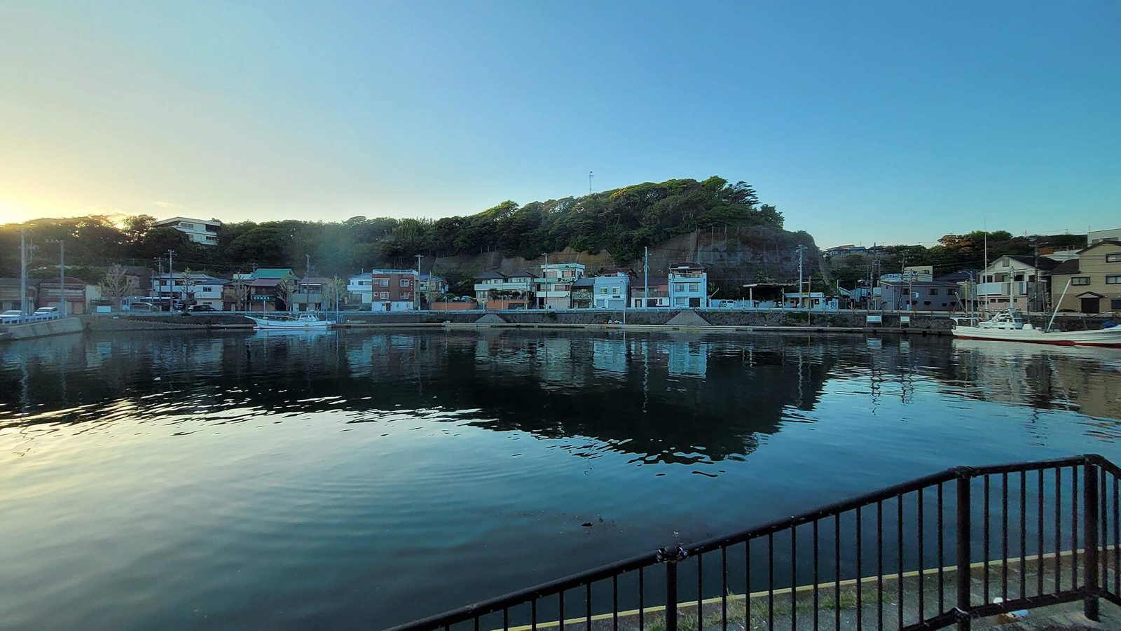 夕暮れの三崎港。水面に建物と山が映り込む漁港の風景